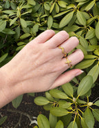 Elevated Faith Christian Jewelry gold rings with cross design worn on a hand among green foliage