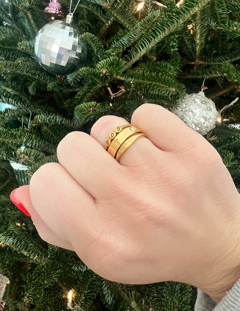 Elevated Faith Christian Jewelry Ring Stack with three gold bands on a hand against a festive background