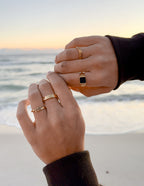 Elevated Faith Christian Jewelry featuring stylish gold rings worn on a beach at sunset