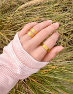 Three gold rings from Elevated Faith, showcasing stylish Christian Jewelry on a hand in natural setting