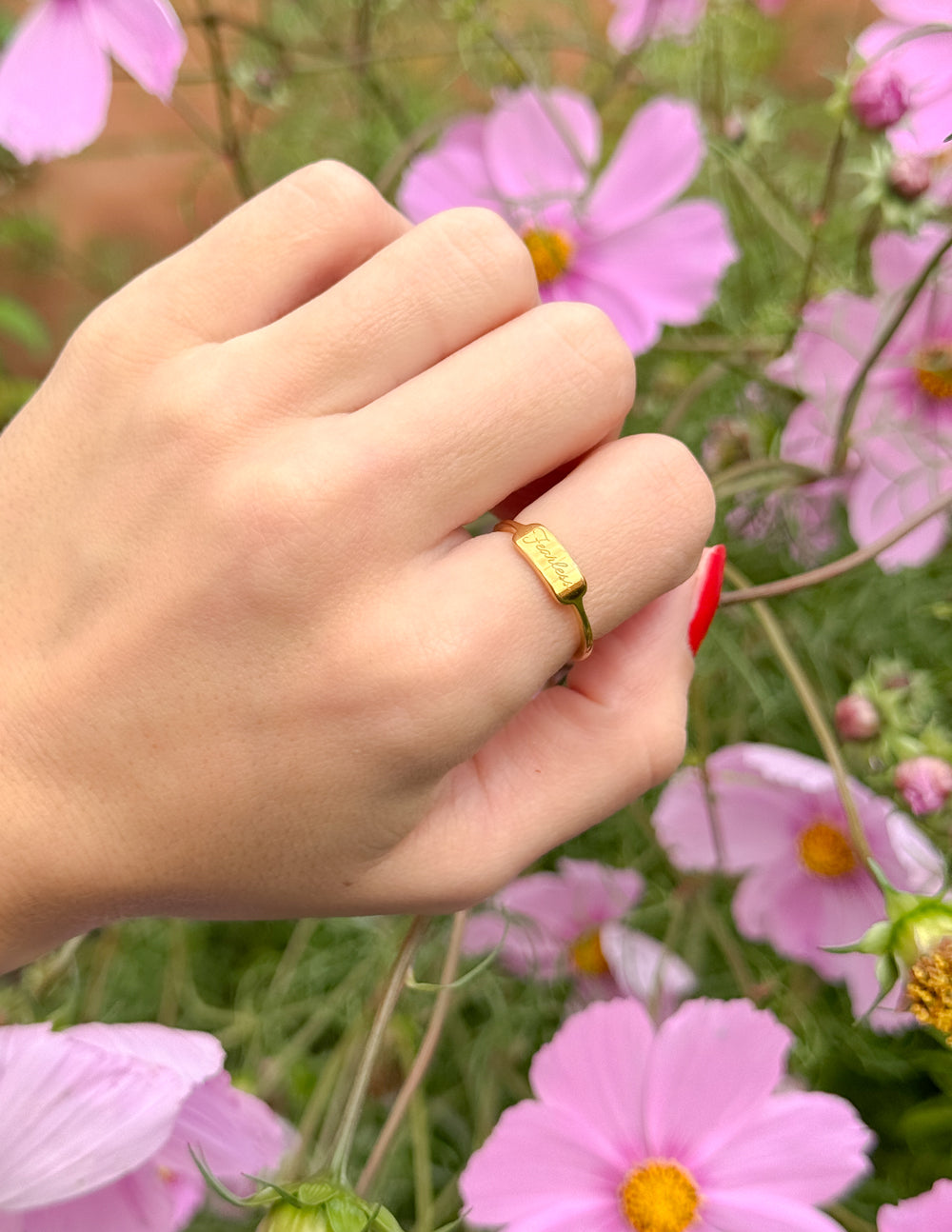 Elevated Faith Gold Ring on Hand among Pink Flowers, showcasing elegant Christian Jewelry