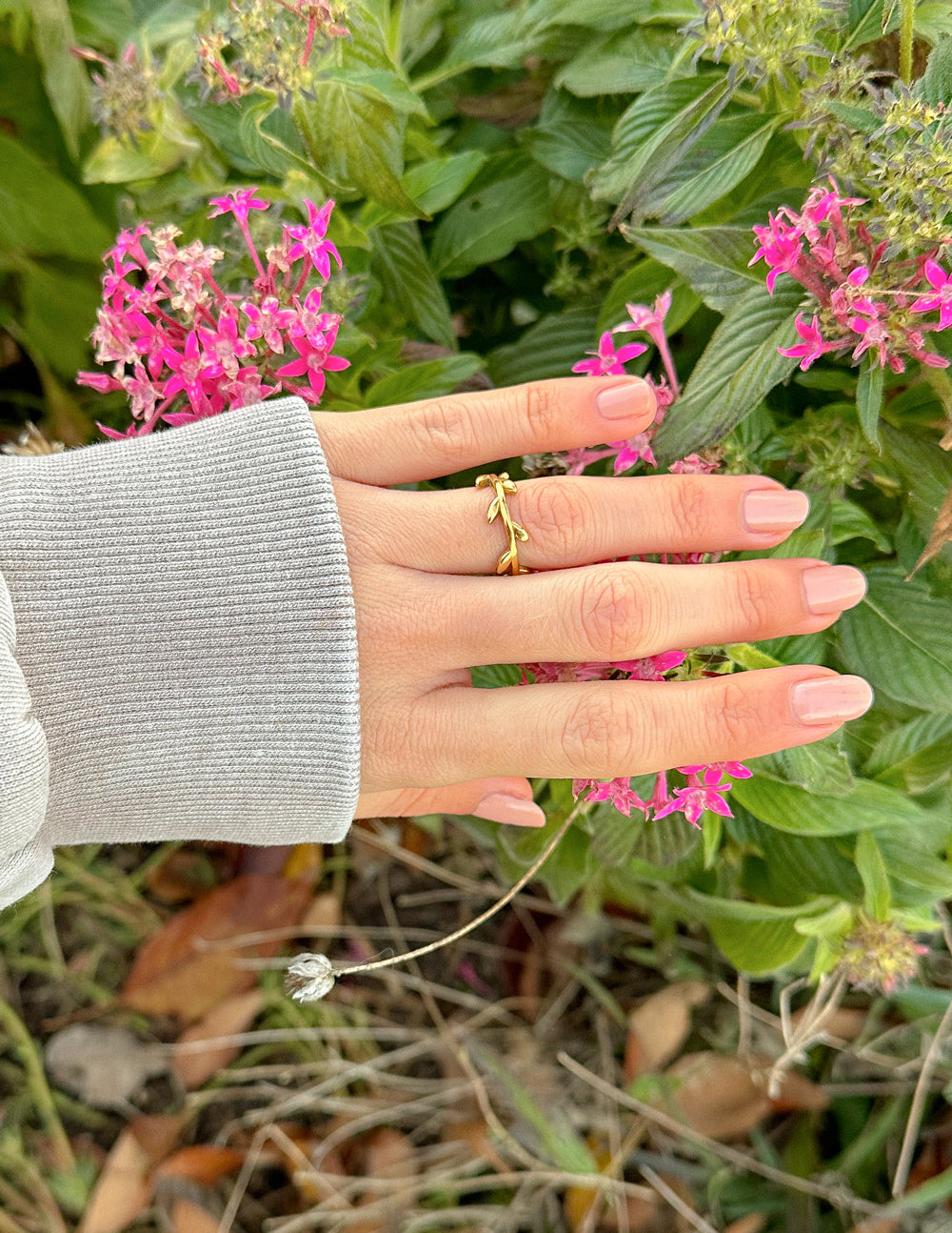 Gold Elevated Faith Ring on a hand surrounded by pink flowers, representing Christian Jewelry