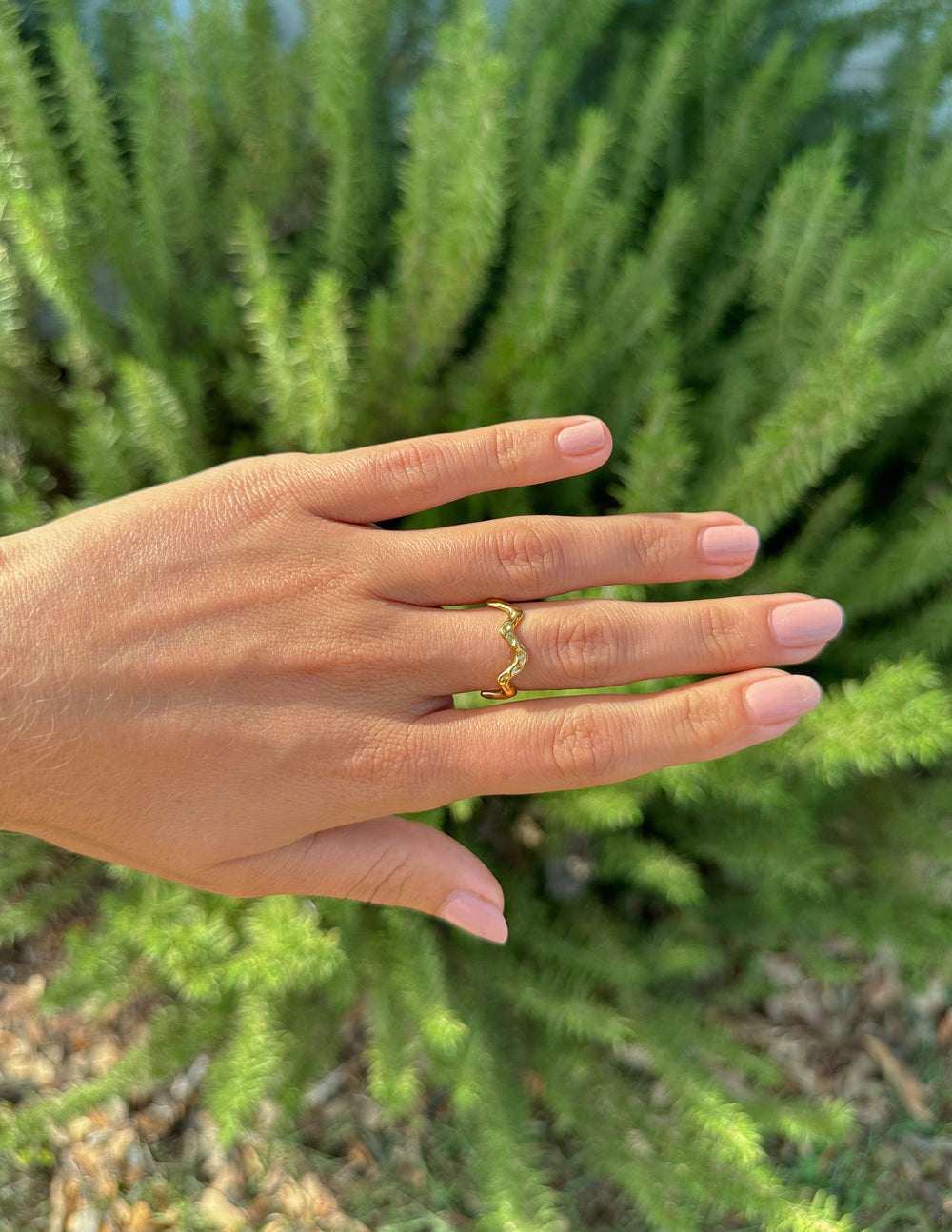 Elegant gold ring on a hand surrounded by greenery, showcasing Elevated Faith Christian Jewelry