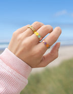 Colorful ring set featuring Christian Jewelry worn on a hand against a beach background