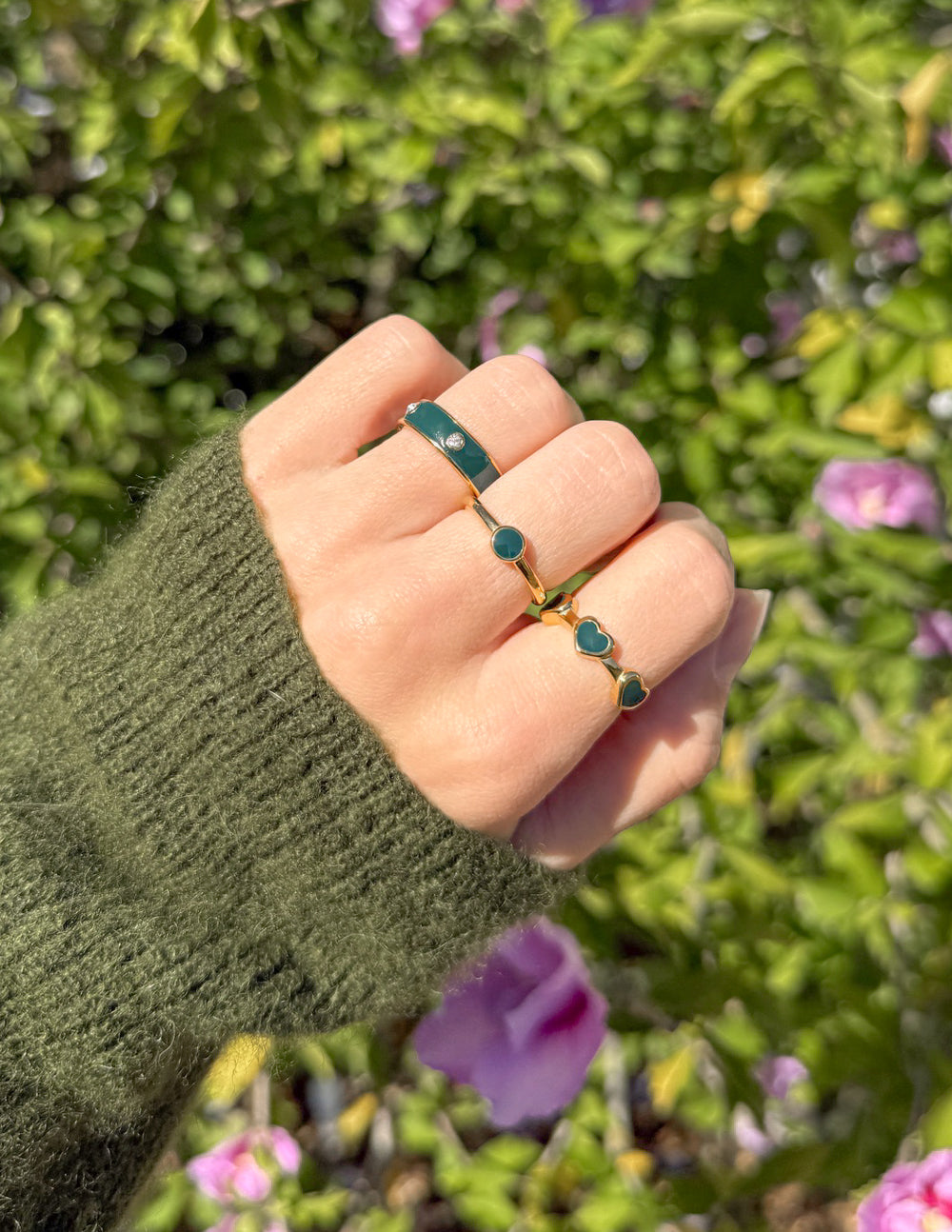 Elevated Faith Christian Jewelry featuring two stylish rings on a hand with a green sweater among flowers