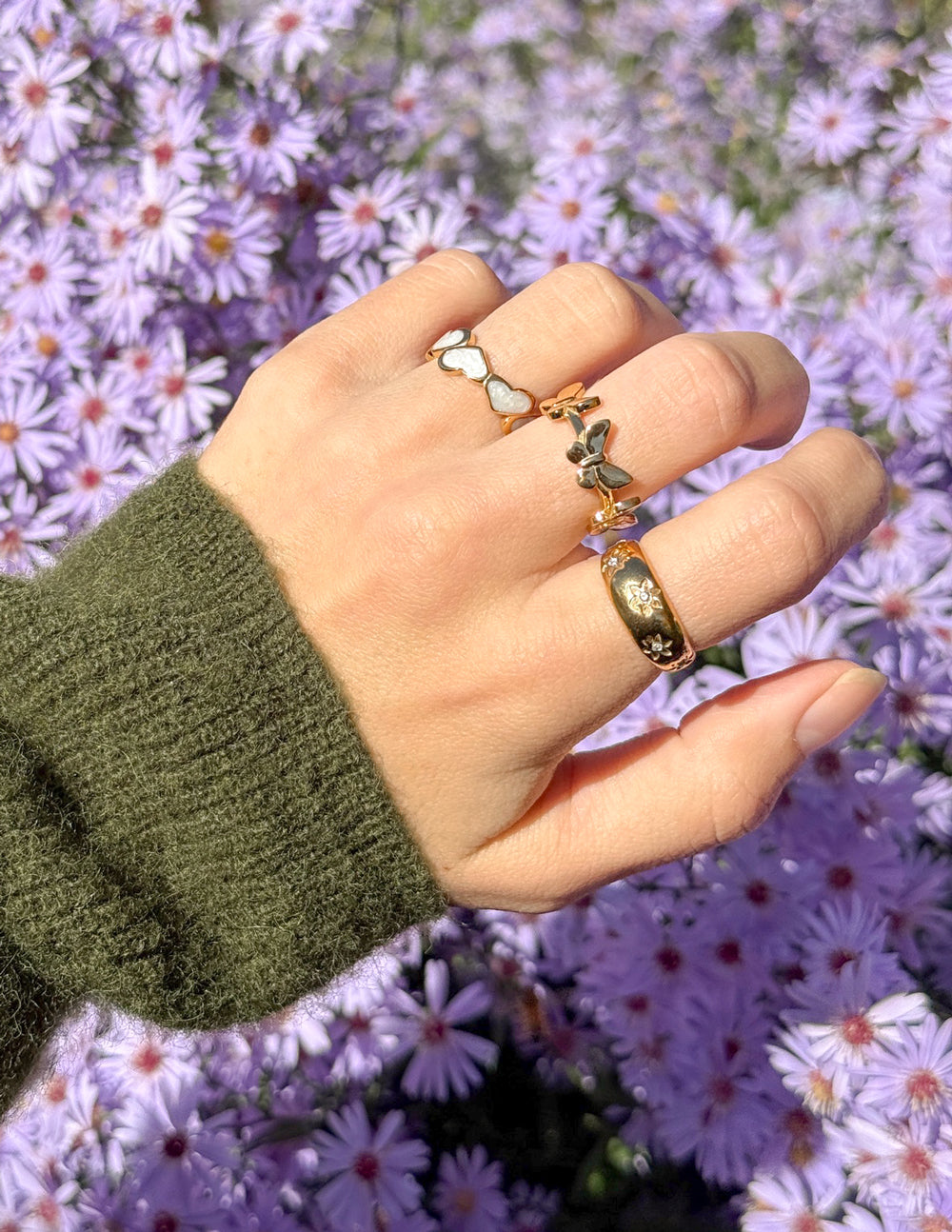 Elegant Elevated Faith Christian Jewelry featuring stacked rings on a hand among purple flowers