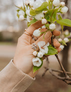 Hand holding flowers wearing Elevated Faith rings, showcasing elegant Christian jewelry