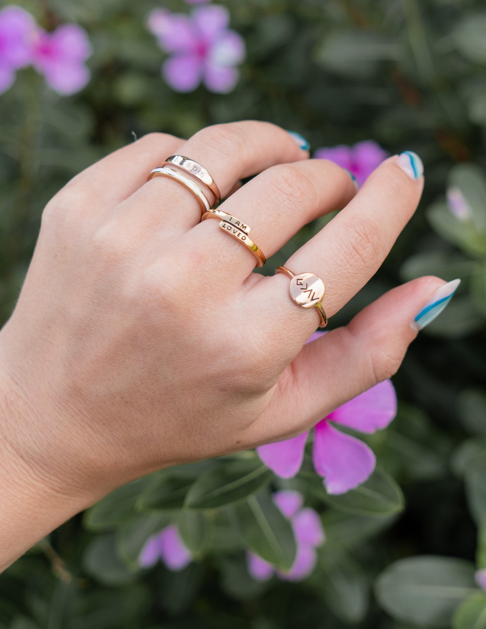 Elevated Faith Christian Jewelry rings displayed on a hand amidst blooming flowers