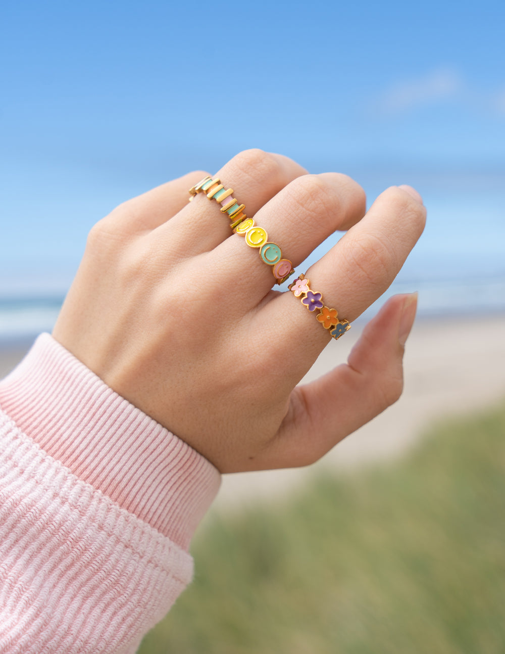 Elevated Faith Christian Jewelry stackable rings in colorful designs worn on a hand outdoors