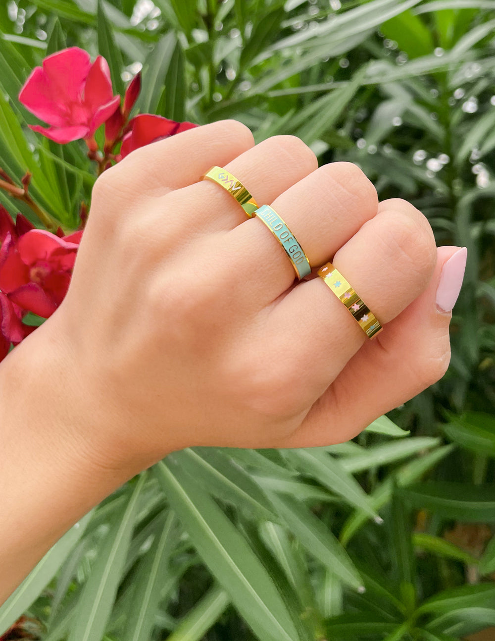 Elevated Faith Christian Jewelry rings in gold and turquoise displayed on a hand surrounded by greenery