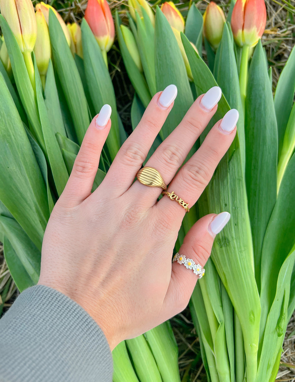 Gold Elevated Faith rings worn on a hand among fresh tulips, representing elegant Christian jewelry