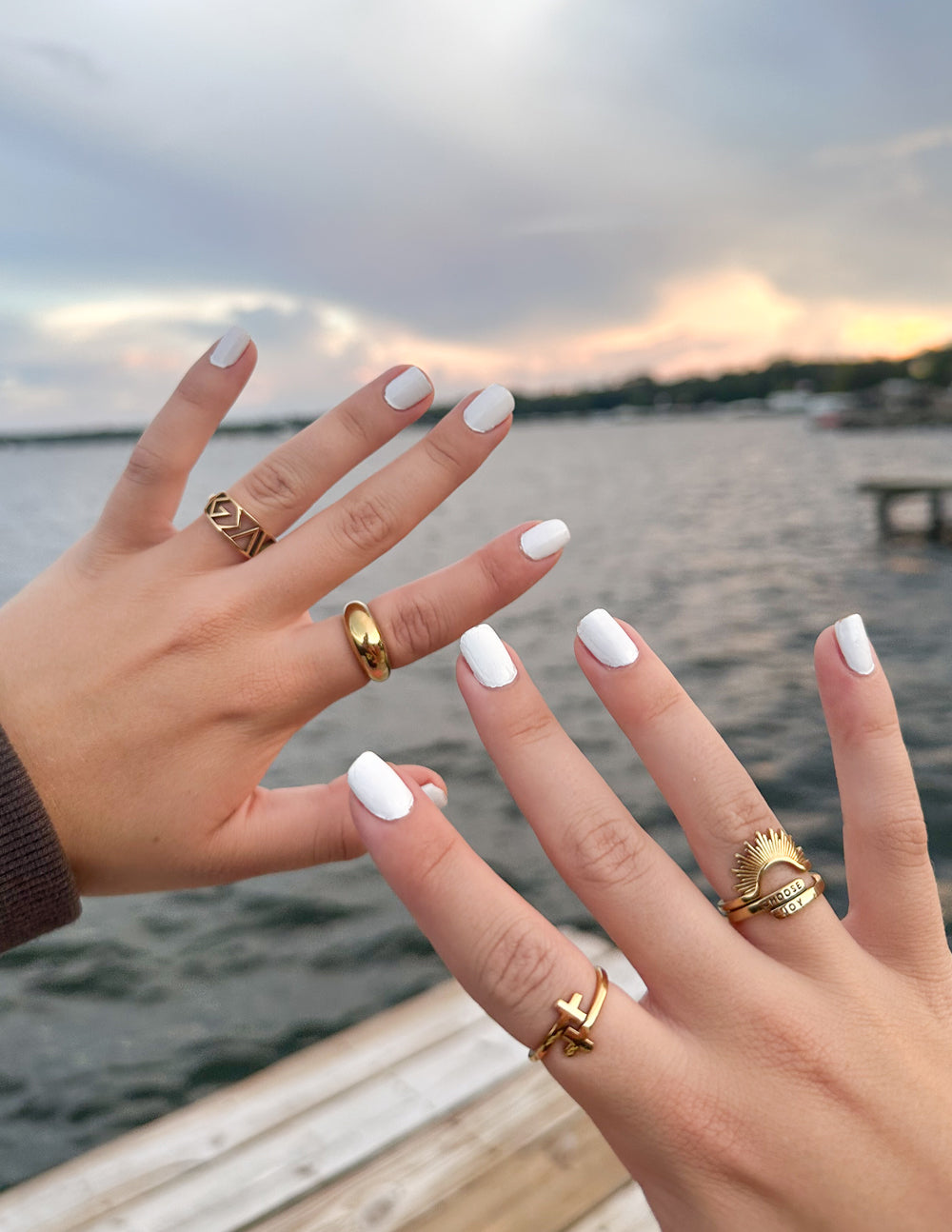 Two hands wearing gold rings showcasing Elevated Faith Christian Jewelry against a scenic waterfront backdrop