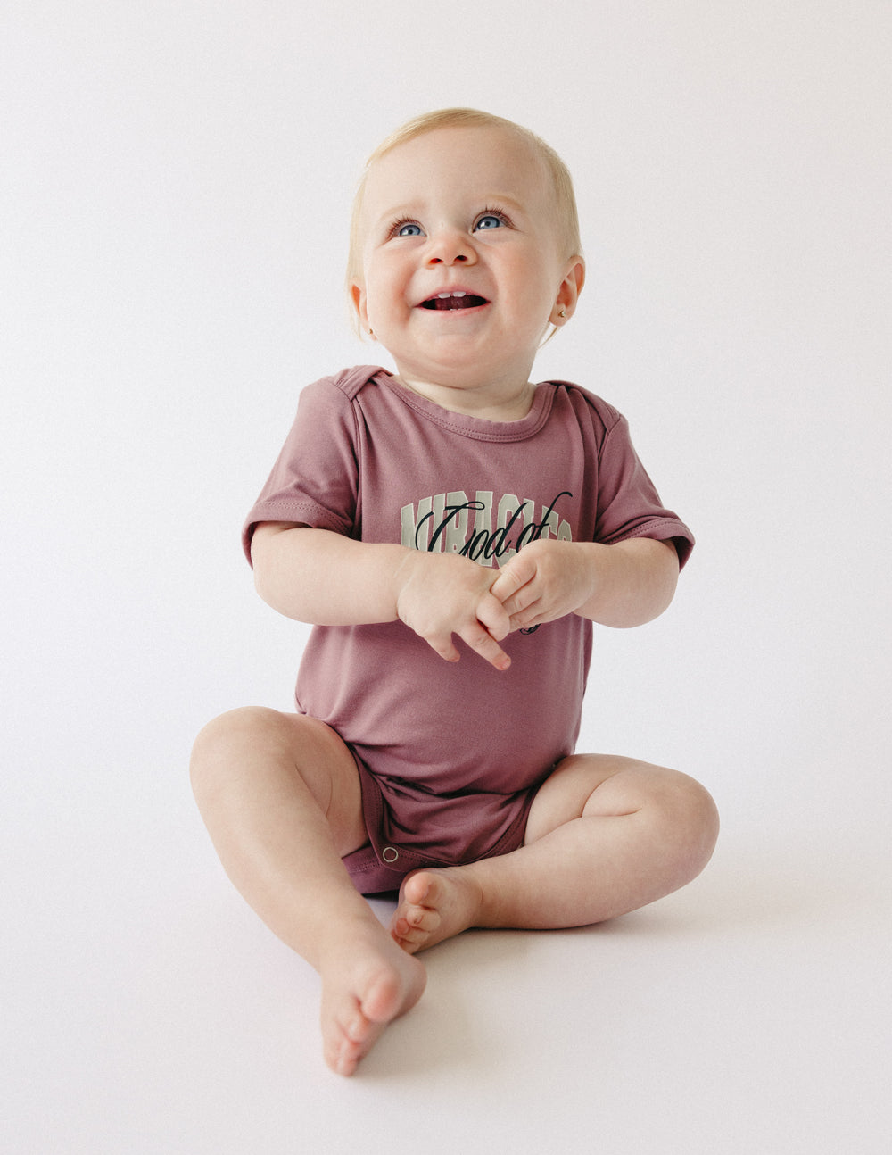 Cute toddler wearing a mauve onesie with a fun design from Elevated Faith, perfect Christian Kids Apparel