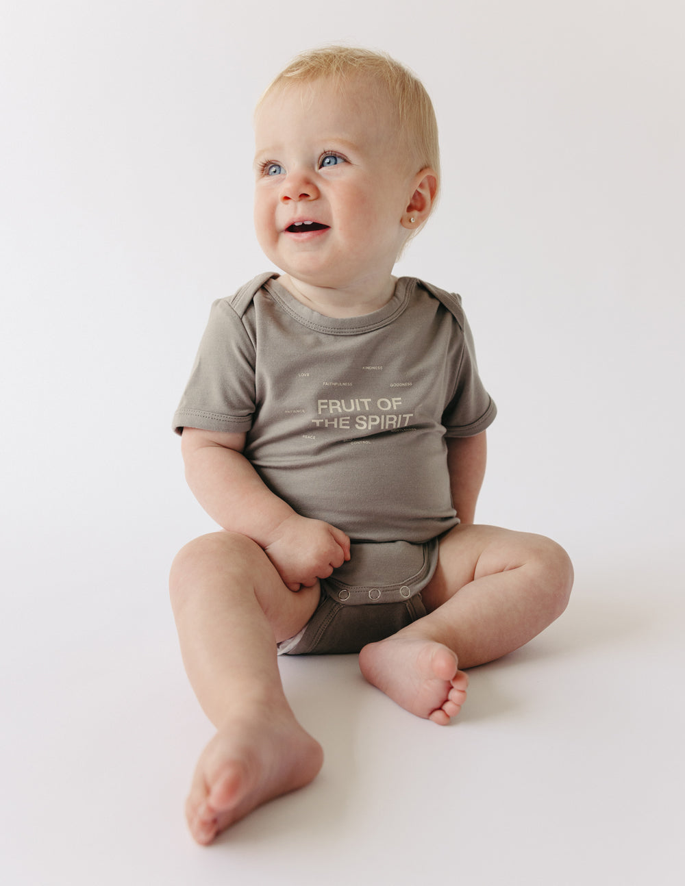 Cute baby in a gray onesie with 'Fruit of the Spirit' design from Elevated Faith, ideal Christian Kids Apparel