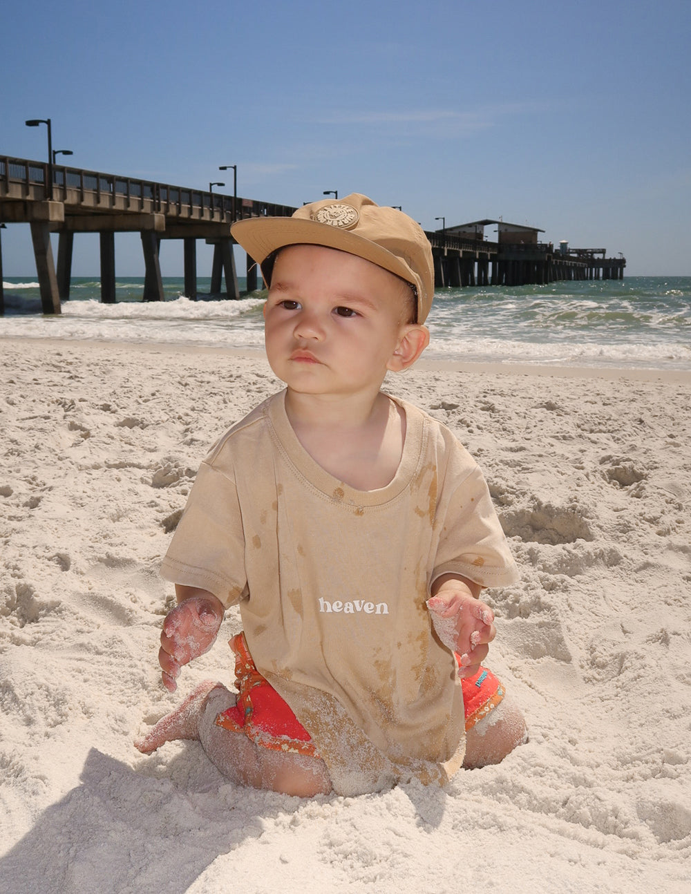 Baby wearing beige t-shirt with the word heaven, ideal for Christian Kids Apparel on the beach
