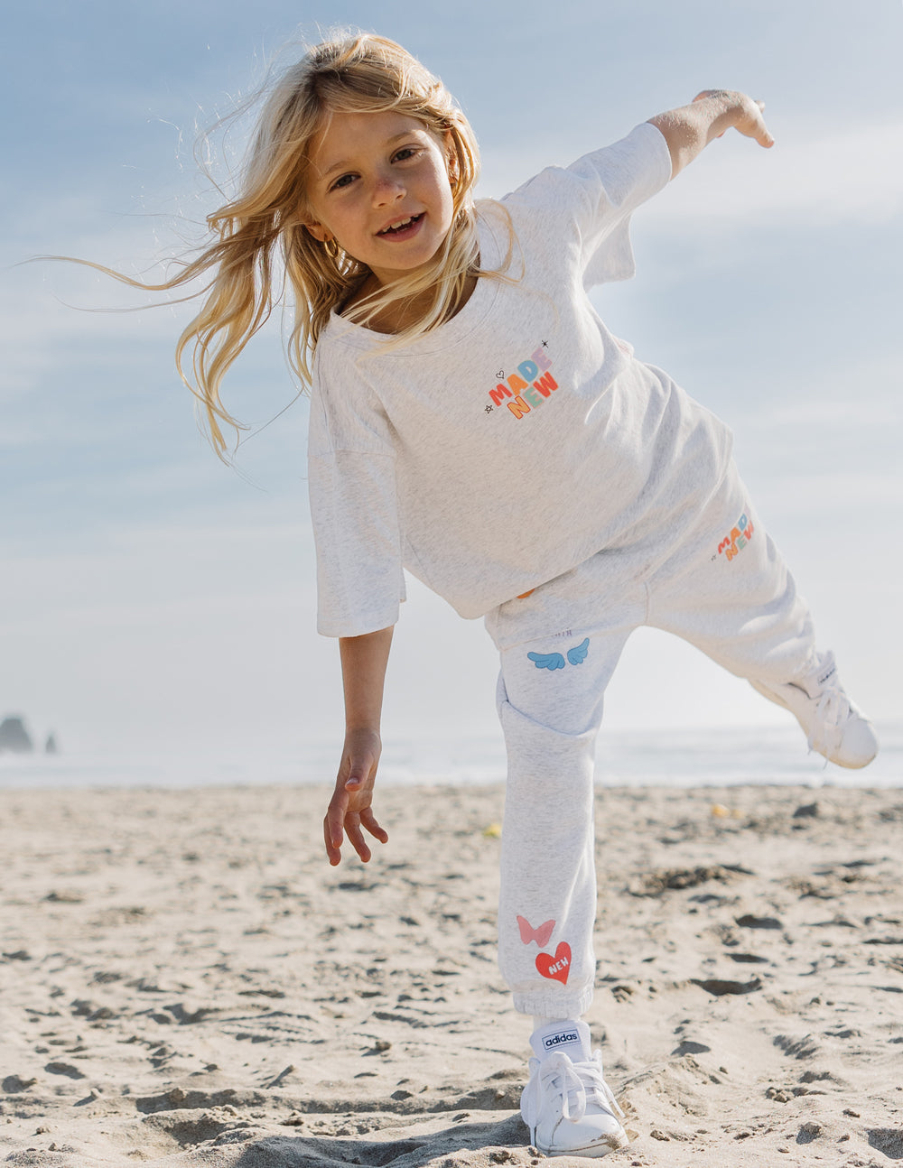 Happy girl in a white kids t-shirt playing on the beach, part of Christian Kids Apparel collection