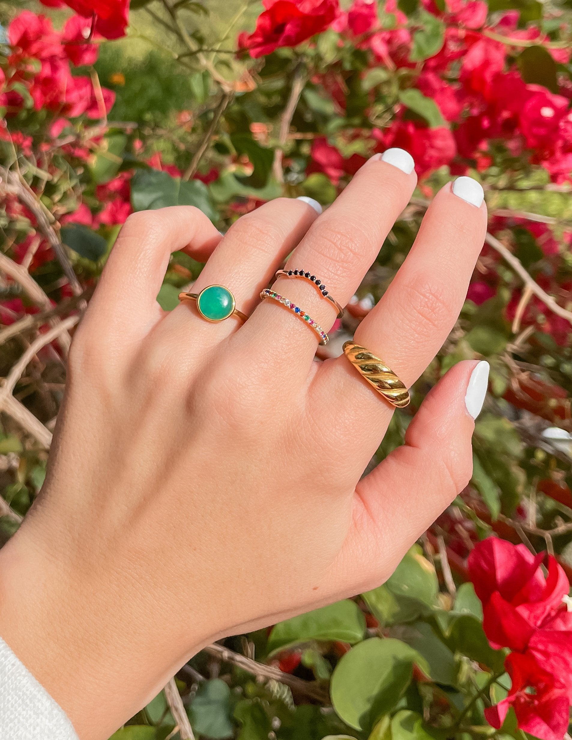 Elevated Faith Christian Jewelry rings featuring vibrant stones stacked on a hand with pink flowers