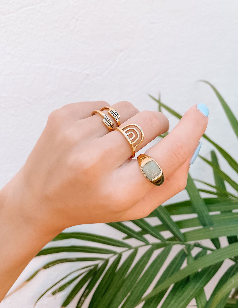 Gold Elevated Faith Christian Jewelry rings displayed on a hand with a palm leaf backdrop