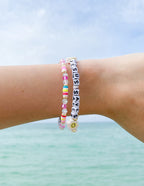 Colorful Elevated Faith Christian Jewelry Bracelet with letter beads spelling 'Jesus Saves' on a wrist by the sea