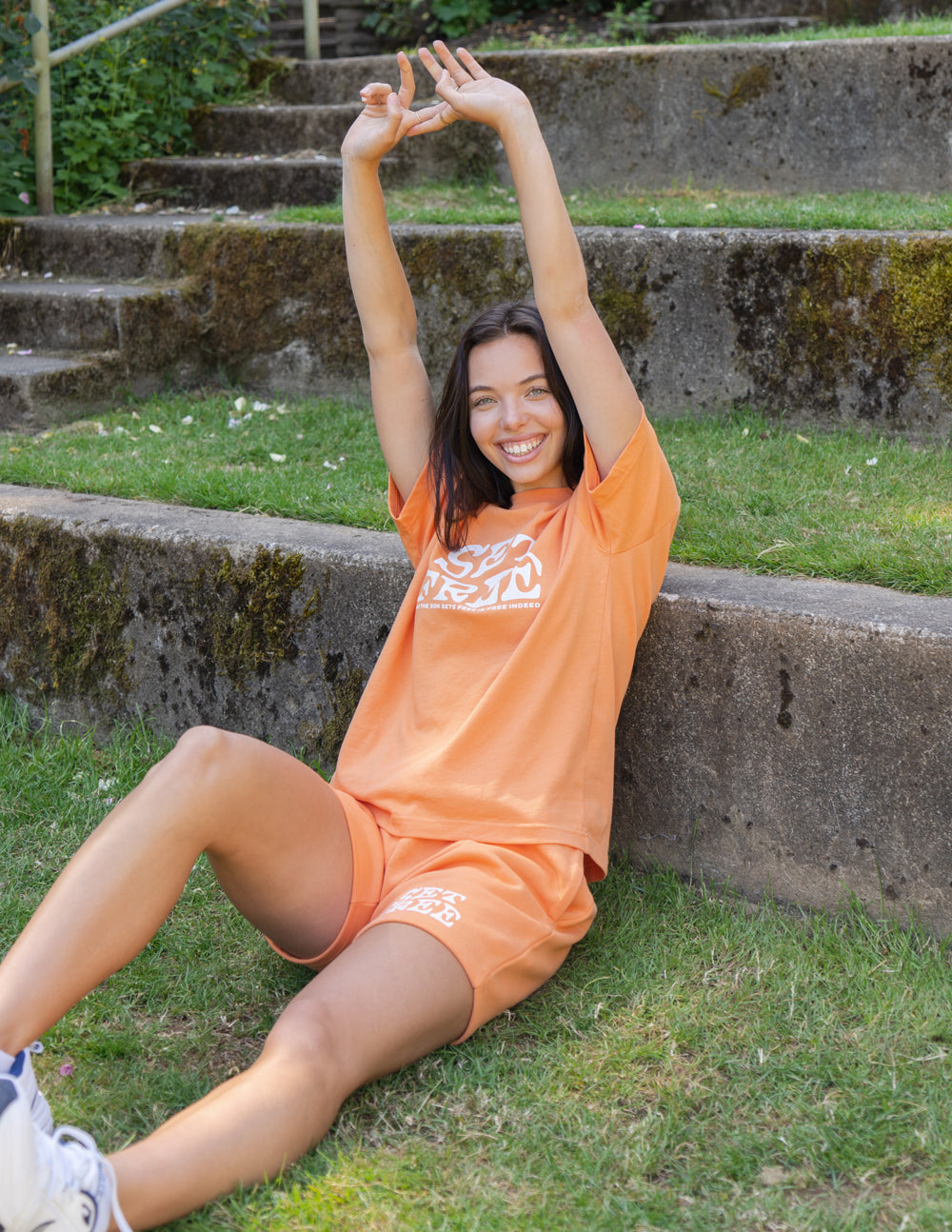 Model wearing Elevated Faith Christian Shorts in orange, styled for casual summer outings