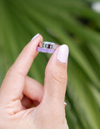 Elevated Faith Christian Jewelry Ring with the word loved engraved, held between fingers against green background