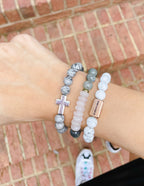 Three stacked bracelets including a cross design, a pink stone, and a Christian Jewelry Bracelet from Elevated Faith